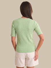 Woman wearing a green ribbed sweater and white shorts on a beige background
