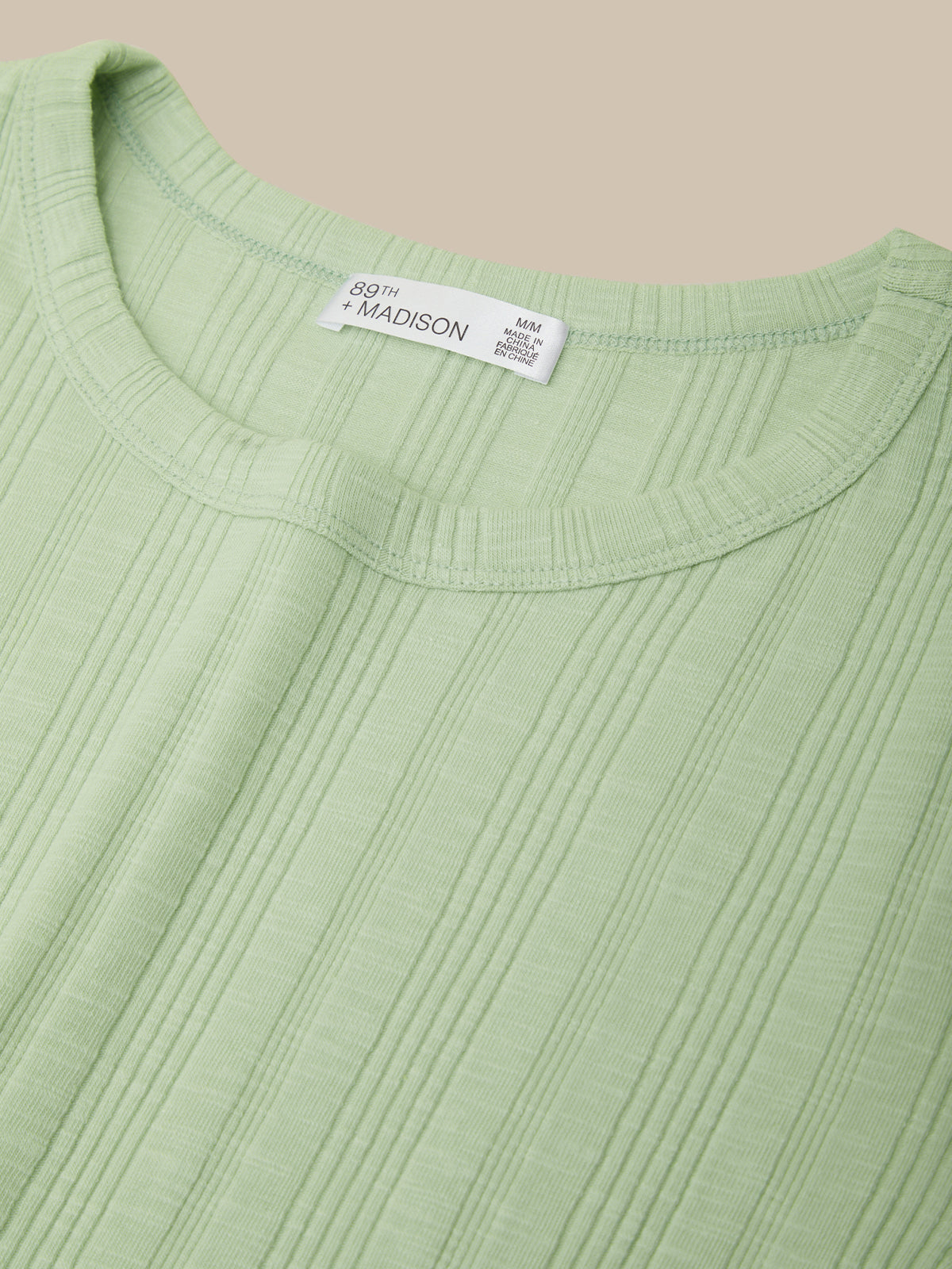 Close-up of a green sweater with a brand label on a beige background
