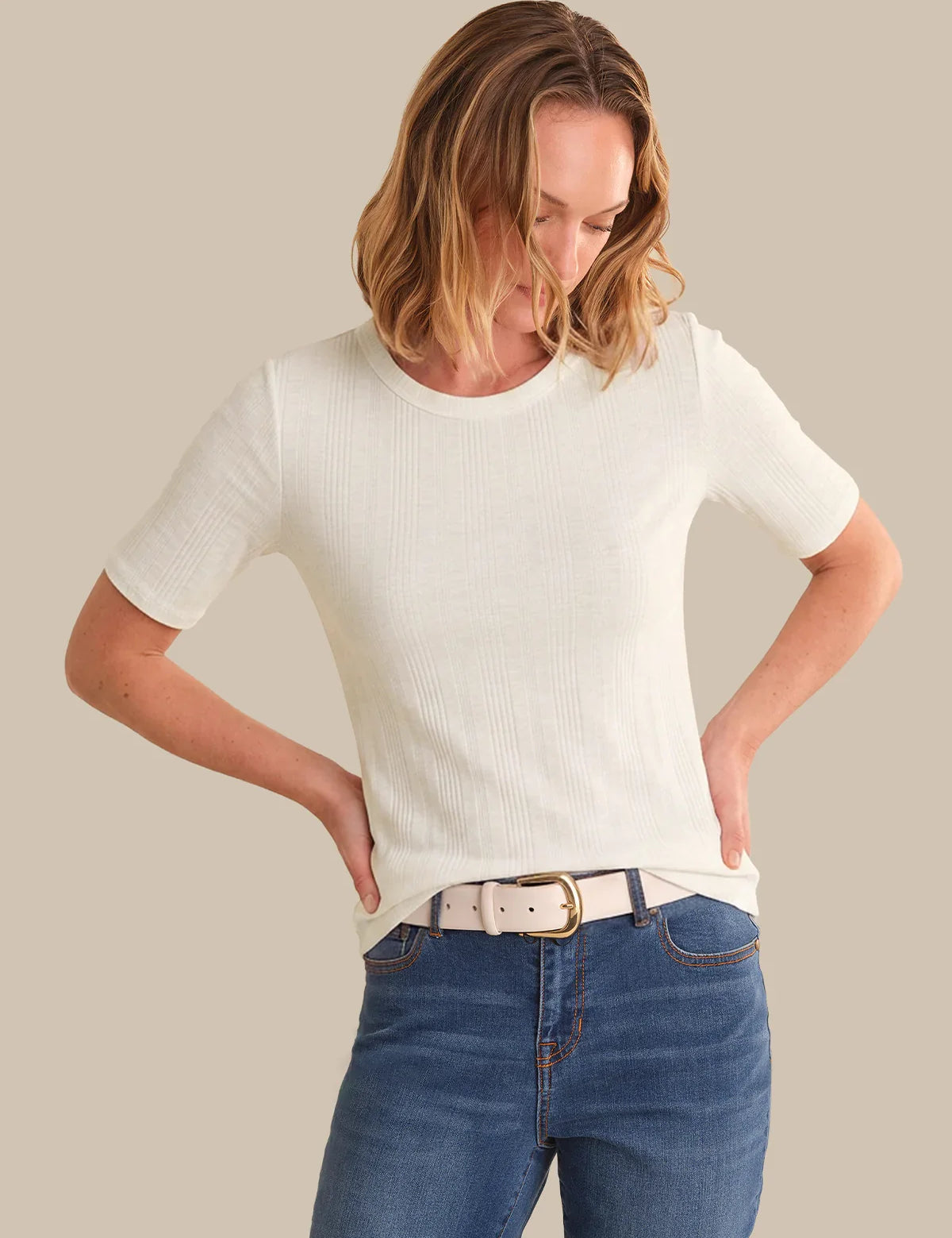 Woman wearing a white t-shirt and blue jeans against a beige background