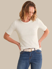 Woman wearing a white t-shirt and blue jeans against a beige background
