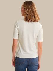 Woman wearing a white ribbed sweater and blue jeans against a beige background
