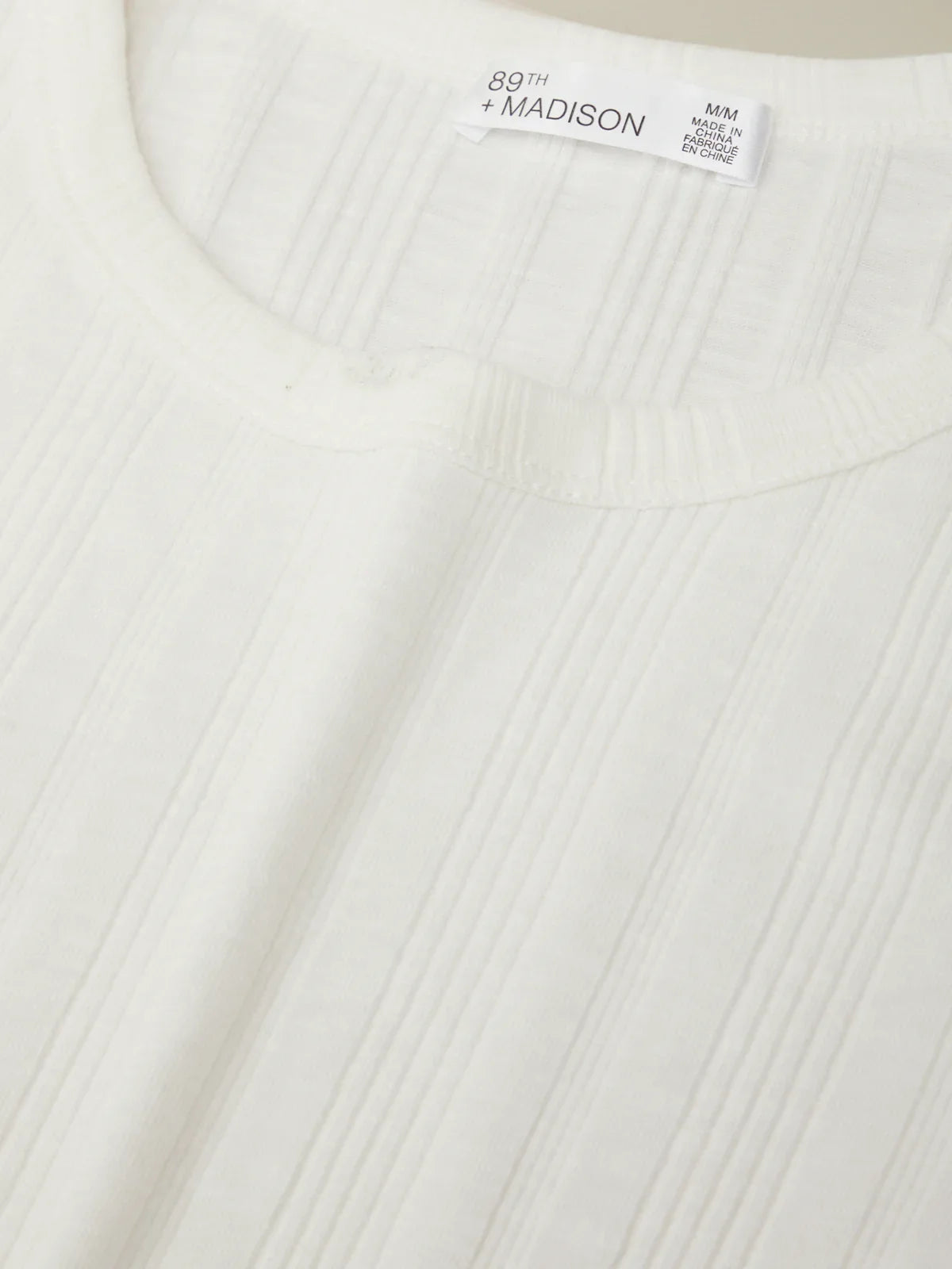 Close-up of a white ribbed sweater with a brand label on a beige background