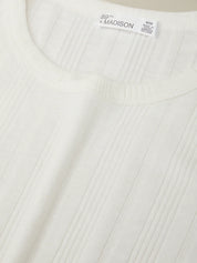 Close-up of a white ribbed sweater with a brand label on a beige background