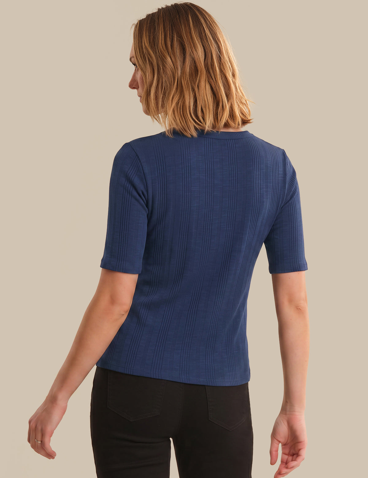 Person wearing a blue ribbed sweater against a beige background