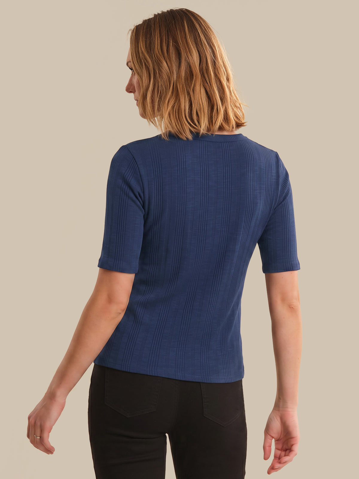 Person wearing a blue ribbed sweater against a beige background