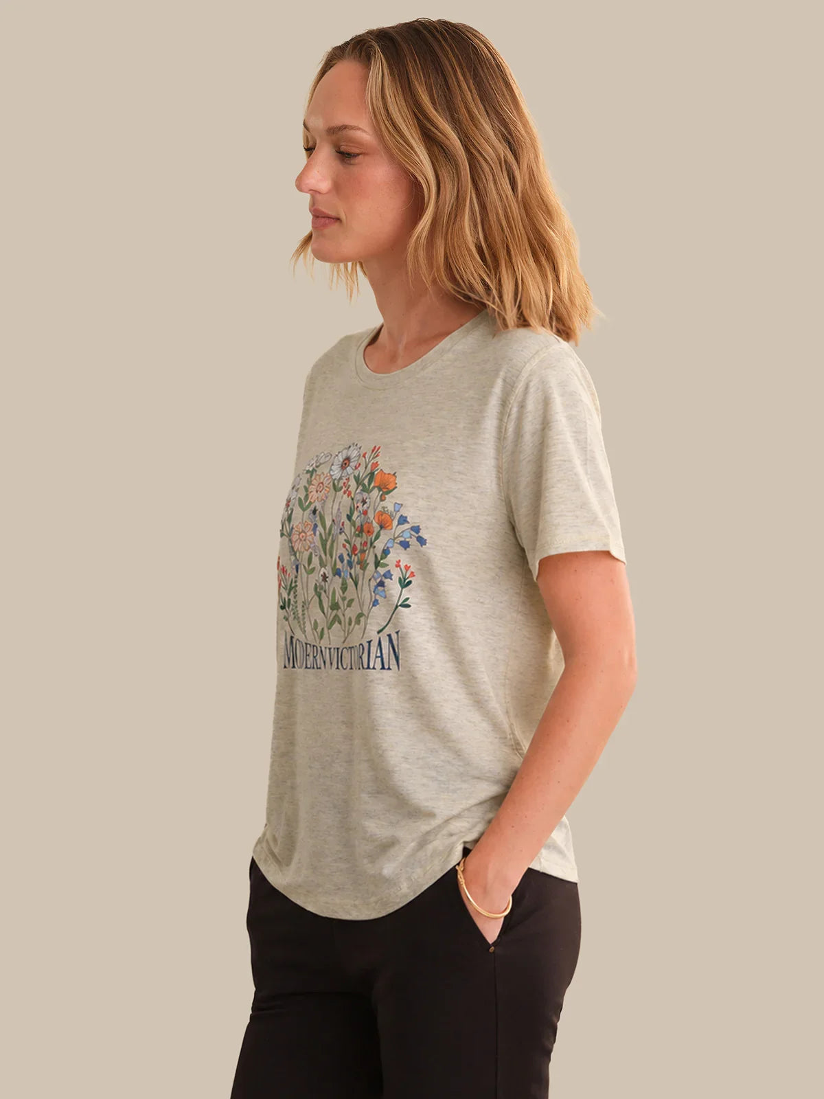 Woman wearing a gray t-shirt with floral design and text on a plain background
