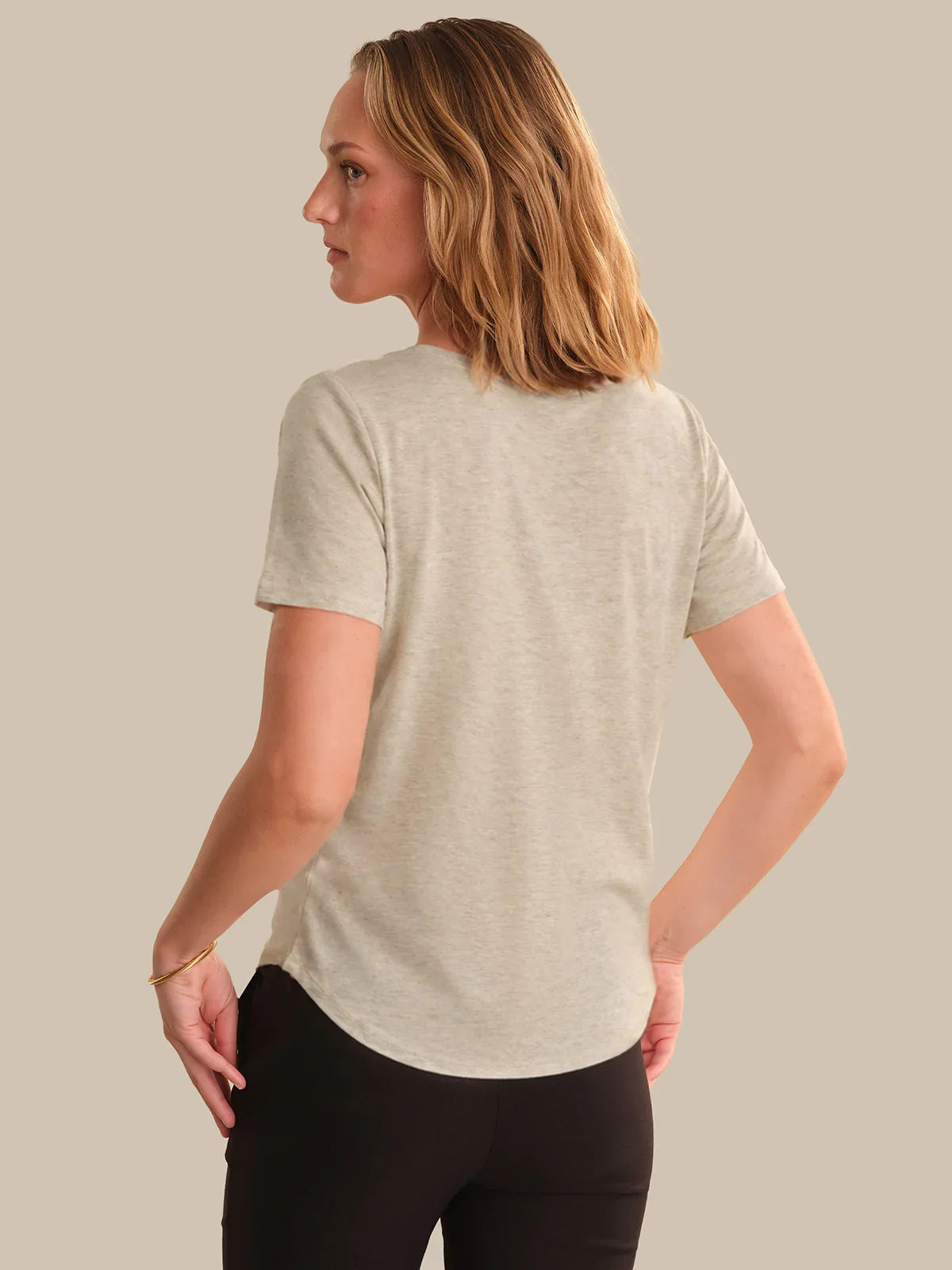 Woman wearing a light gray t-shirt and black pants against a beige background