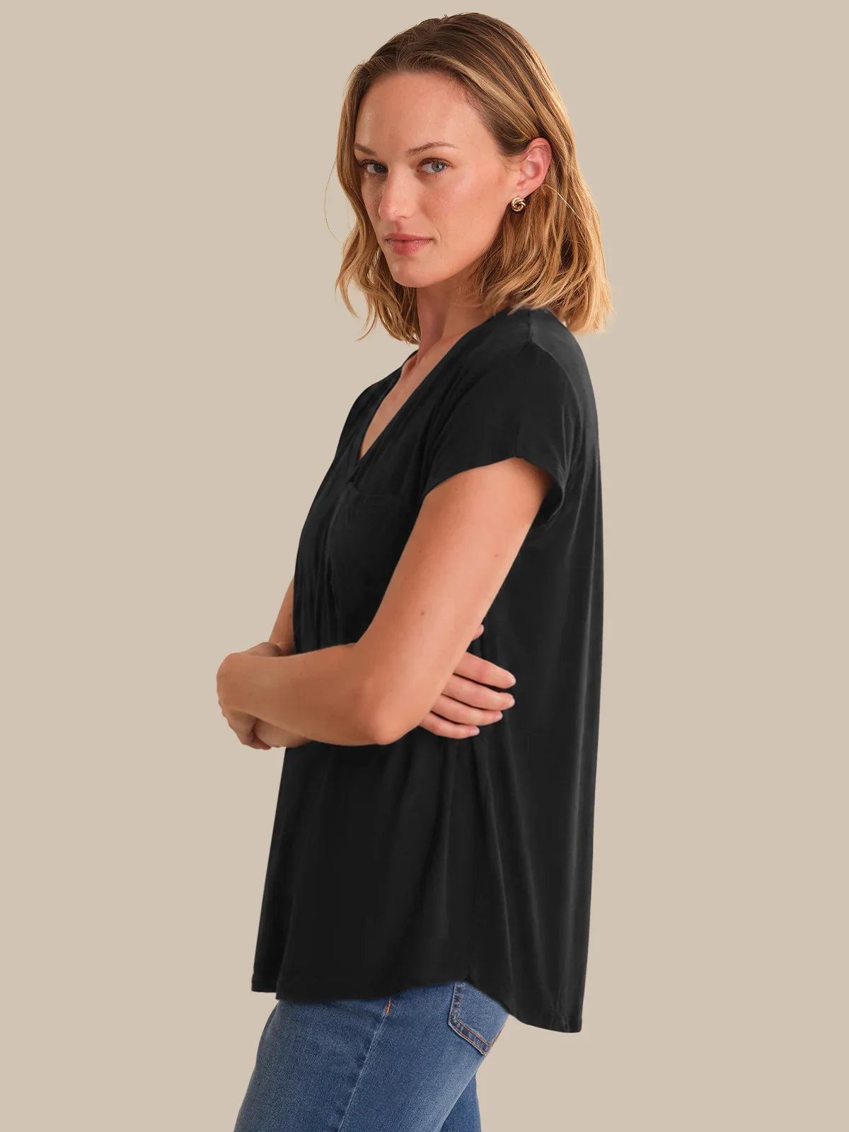 Woman wearing a black t-shirt and blue jeans against a beige background