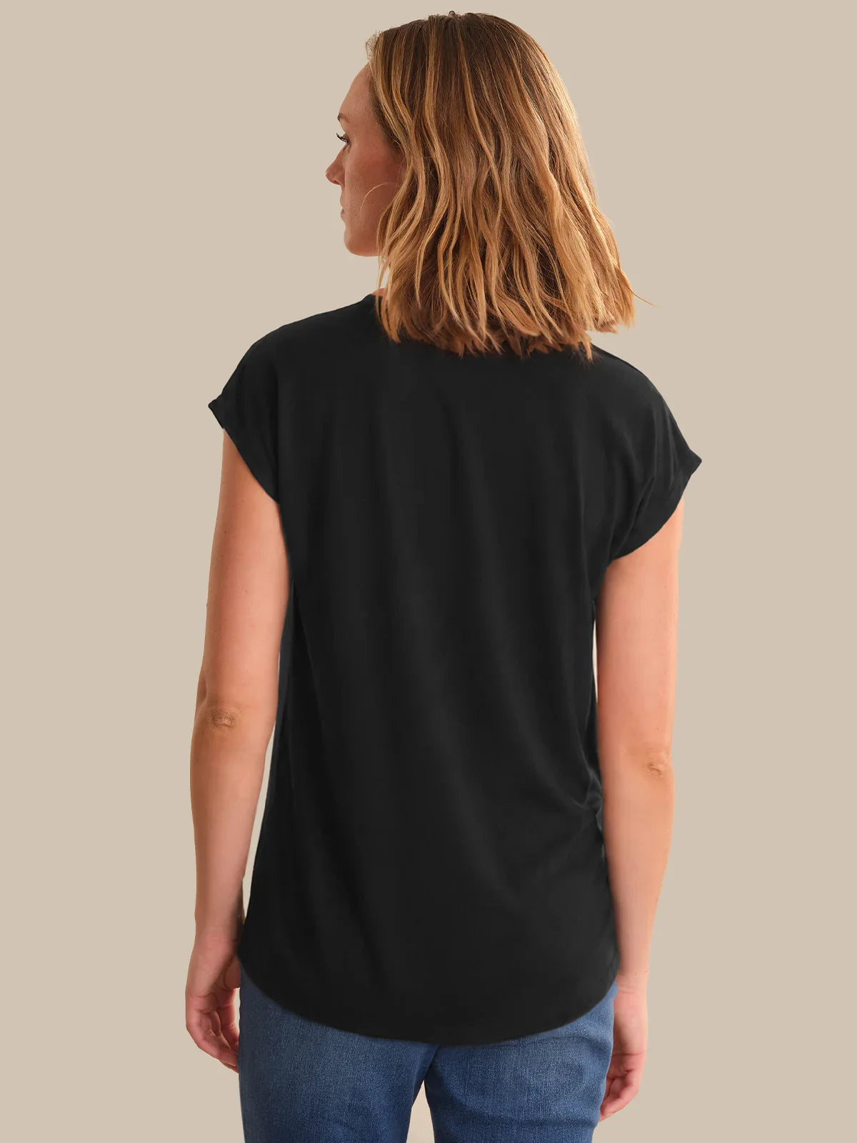 Woman wearing a black t-shirt and blue jeans on a beige background