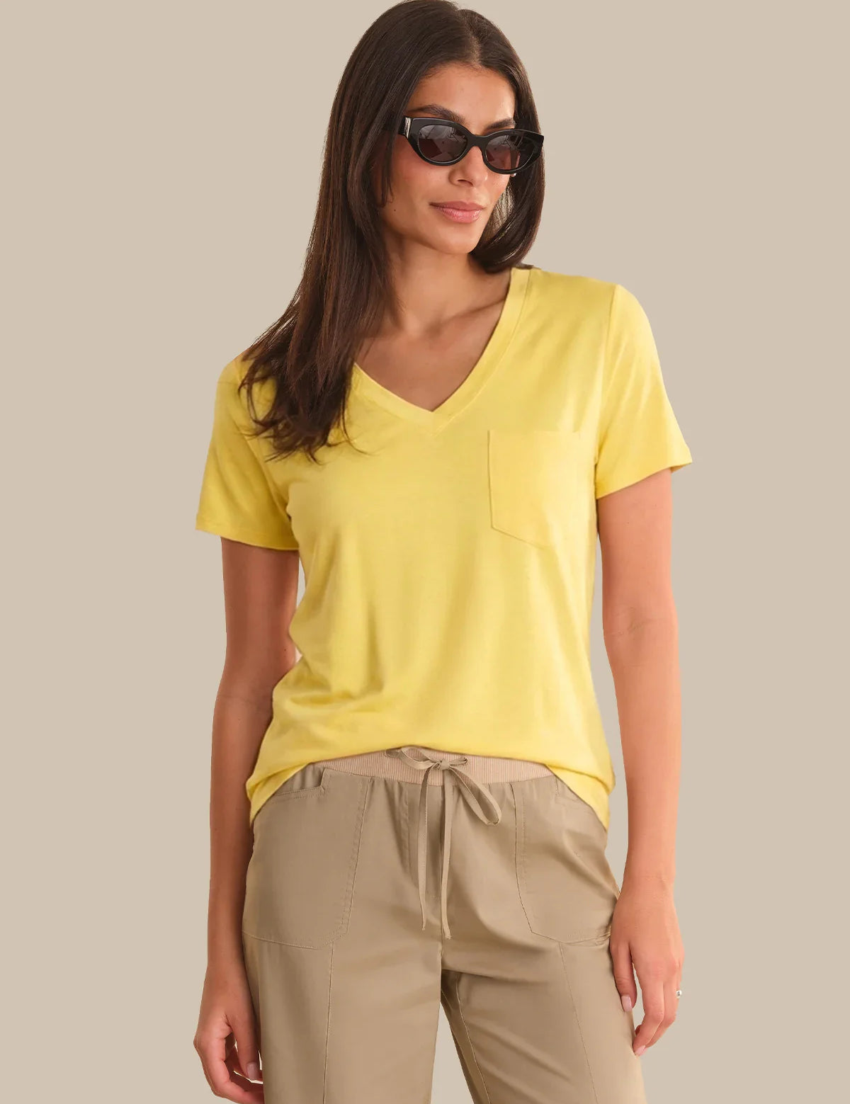 Woman wearing a yellow shirt and beige pants against a neutral background