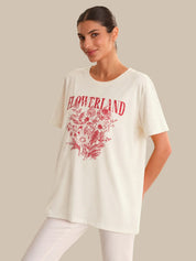 Woman wearing a white t-shirt with red floral design and 'FLOWERLAND' text on a beige background
