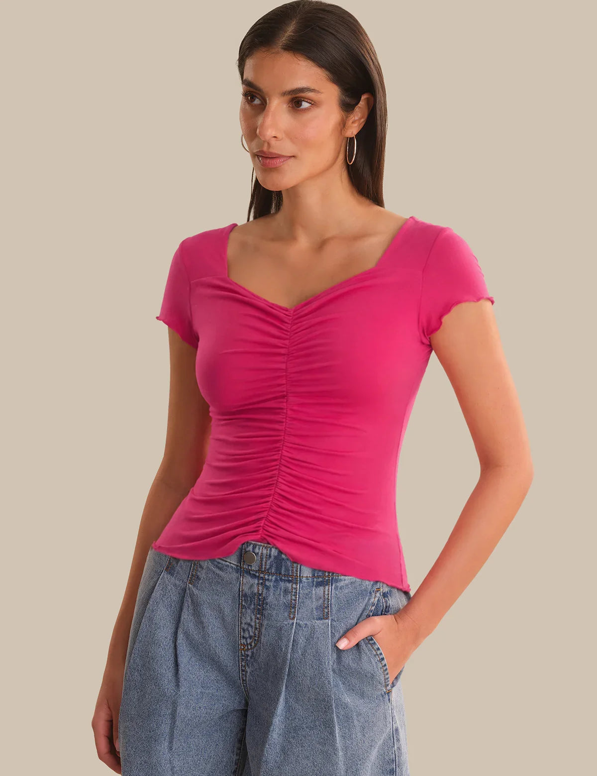 Woman wearing a pink ruched top and blue jeans on a beige background