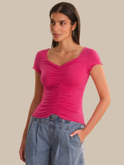 Woman wearing a pink ruched top and blue jeans on a beige background