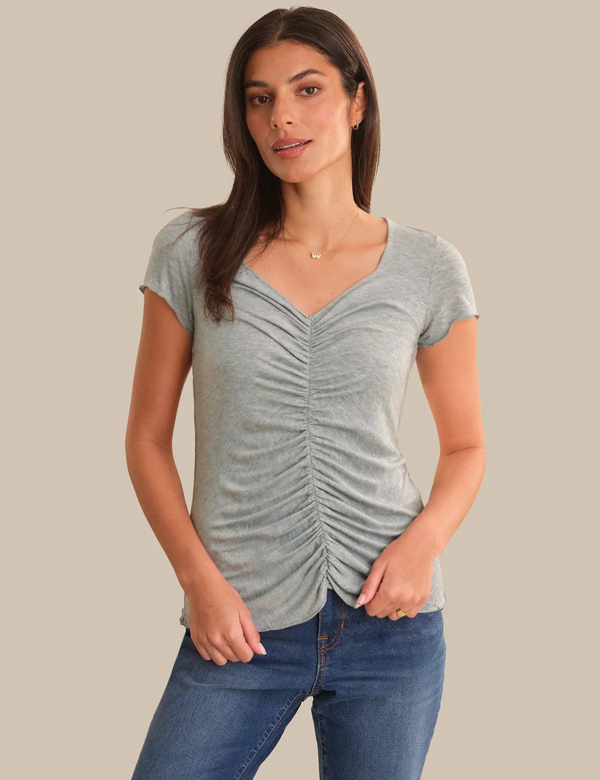 Woman wearing a gray ruched t-shirt and blue jeans on a beige background