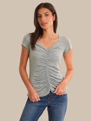 Woman wearing a gray ruched t-shirt and blue jeans on a beige background