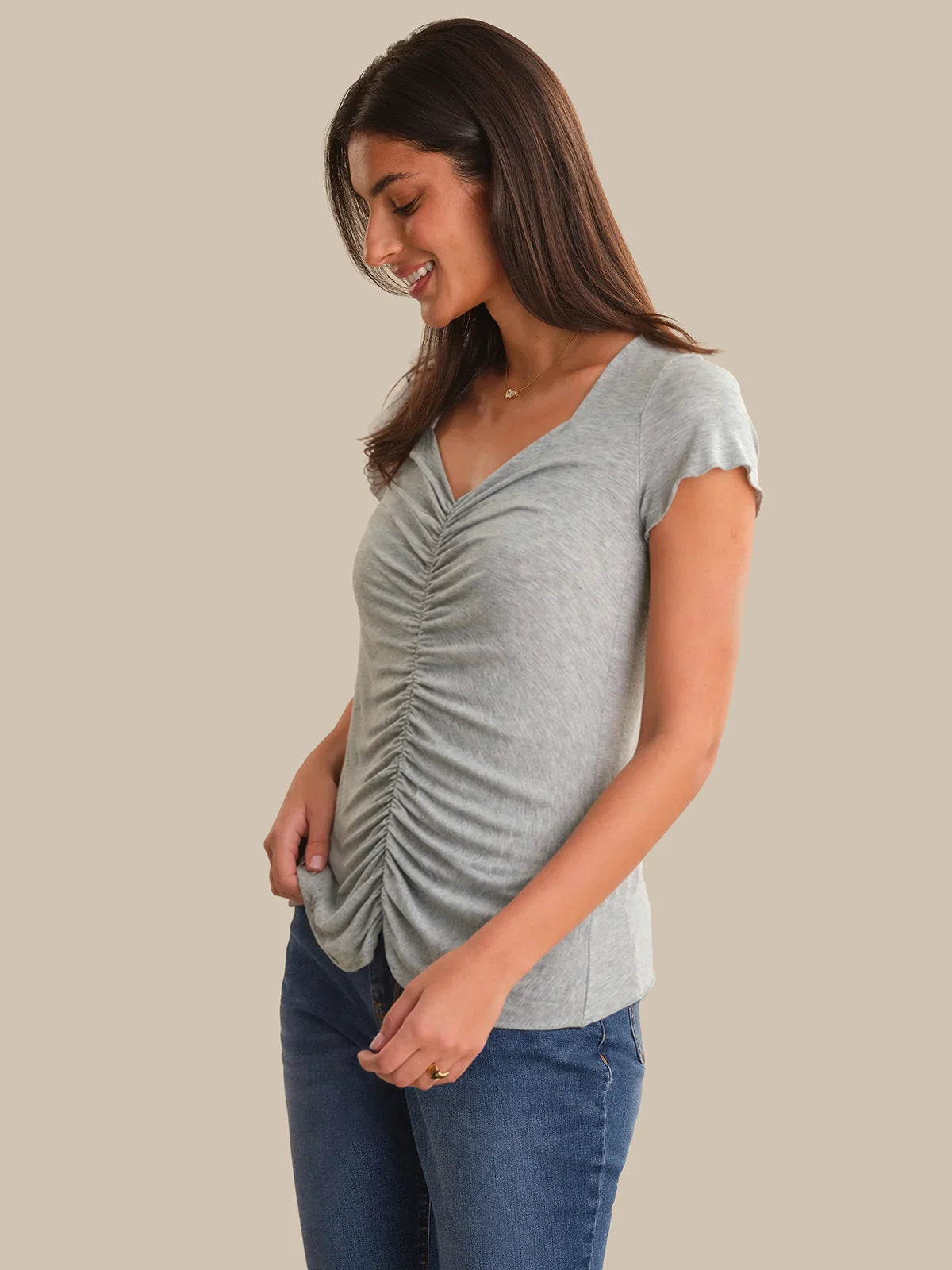 Woman wearing a gray ruched t-shirt and blue jeans on a beige background