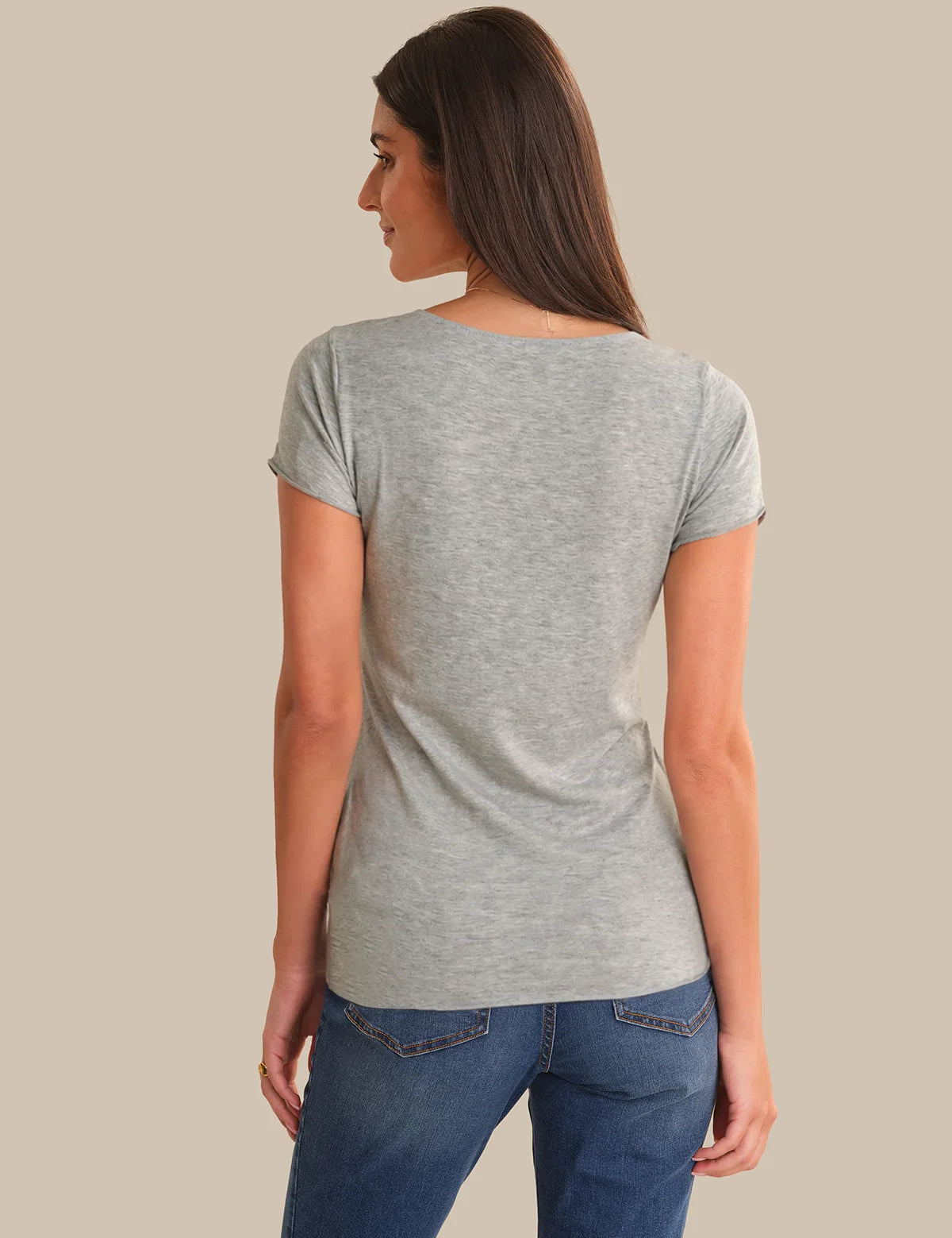 Woman wearing a gray t-shirt and blue jeans against a beige background