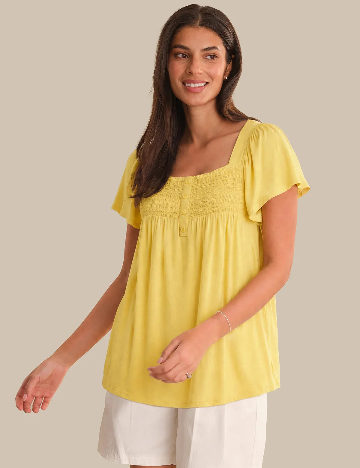 Woman wearing a yellow top and white pants on a beige background