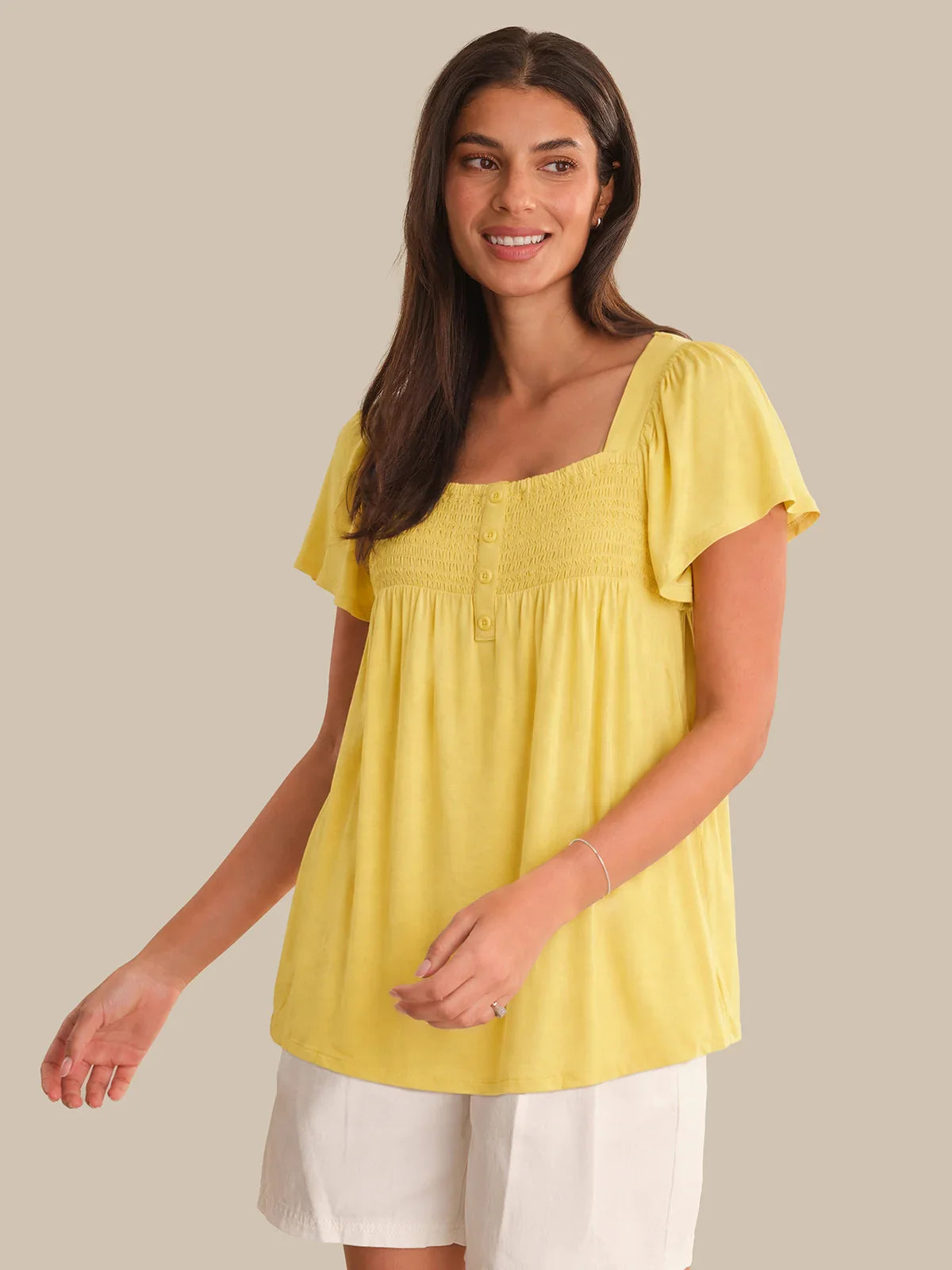Woman wearing a yellow top and white pants on a beige background