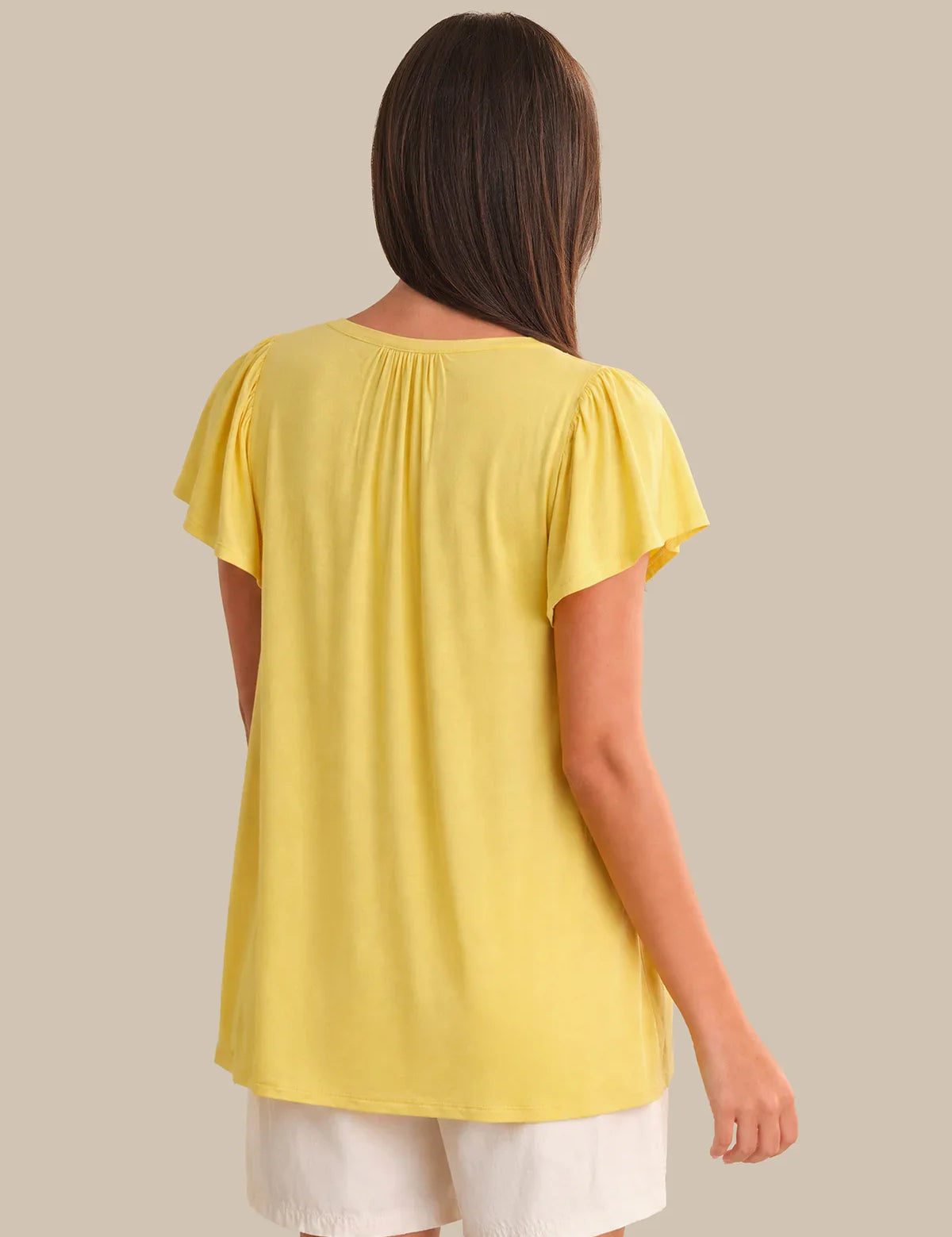 Woman wearing a yellow top and white shorts on a beige background