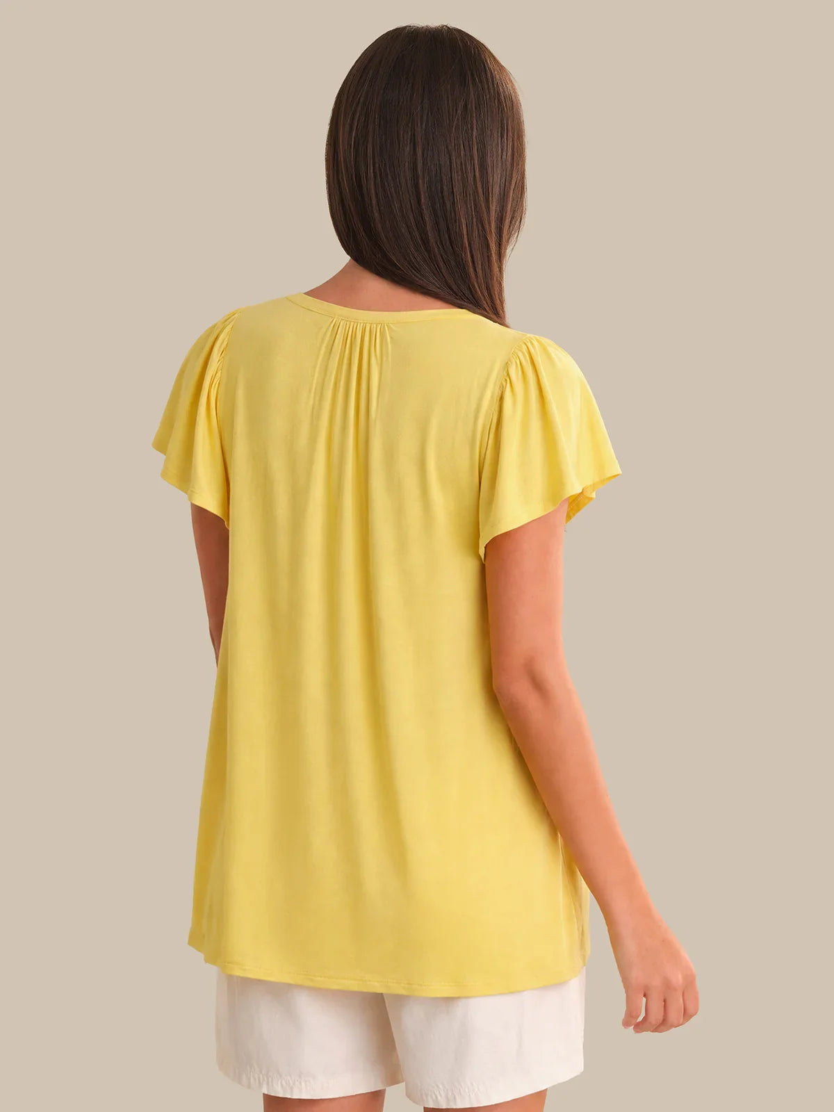 Woman wearing a yellow top and white shorts on a beige background