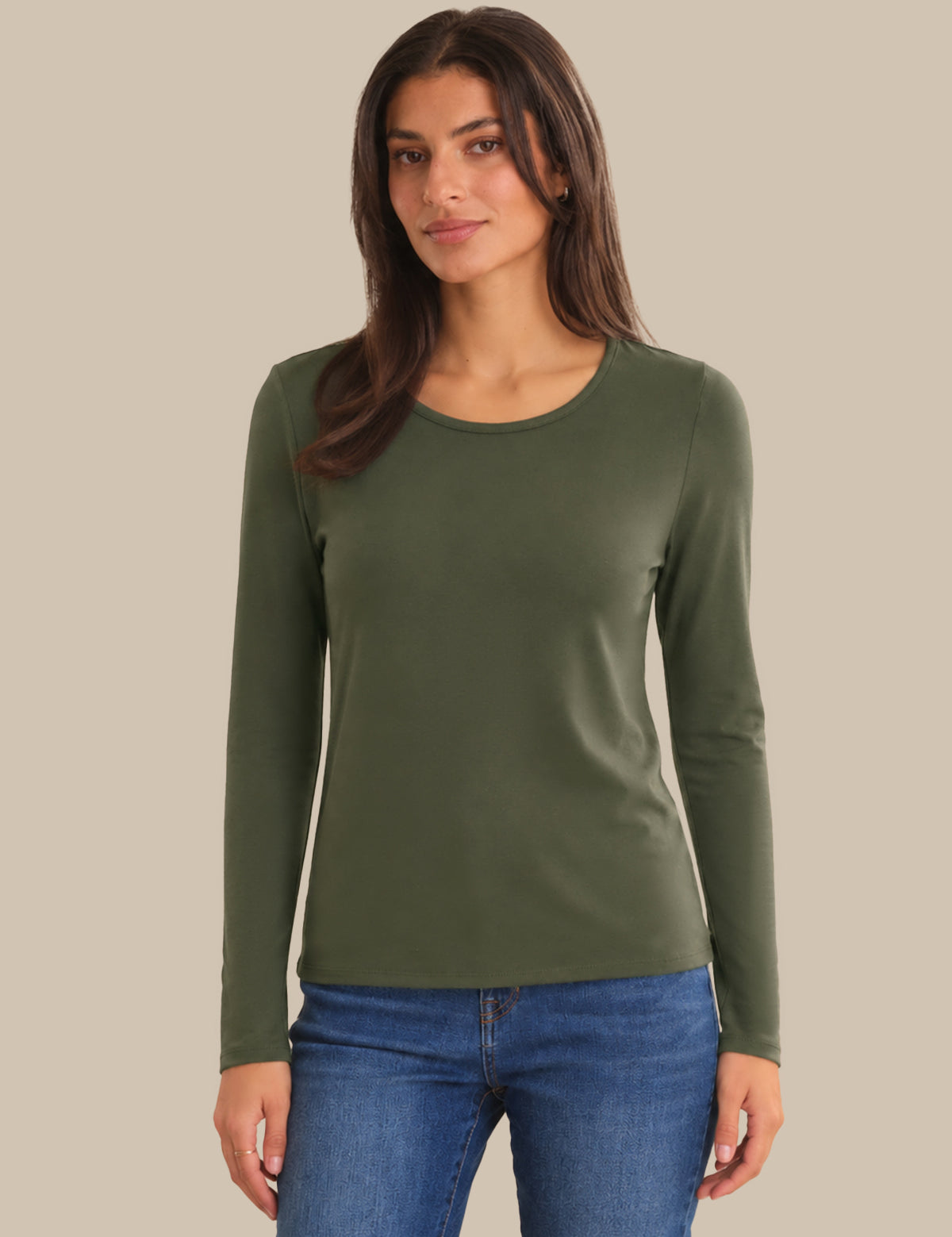A woman modeling a fitted long-sleeve crewneck top in olive green, paired with blue jeans, against a solid beige background.