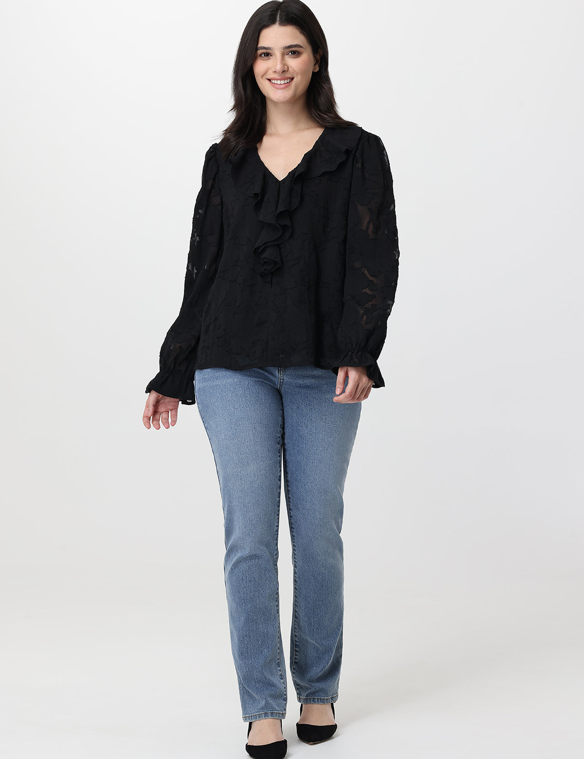 Woman wearing a black blouse with ruffles and light blue jeans on a white background