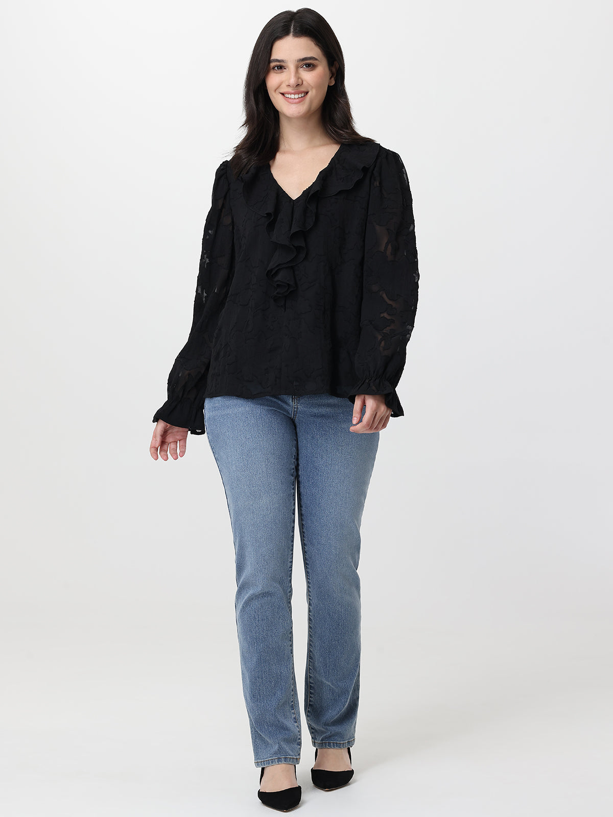 Woman wearing a black blouse with ruffles and light blue jeans on a white background