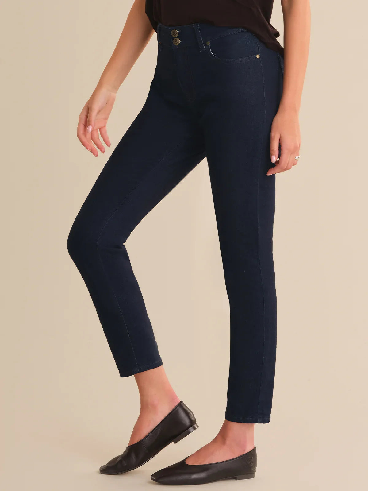 Person wearing dark blue jeans and black shoes on a beige background