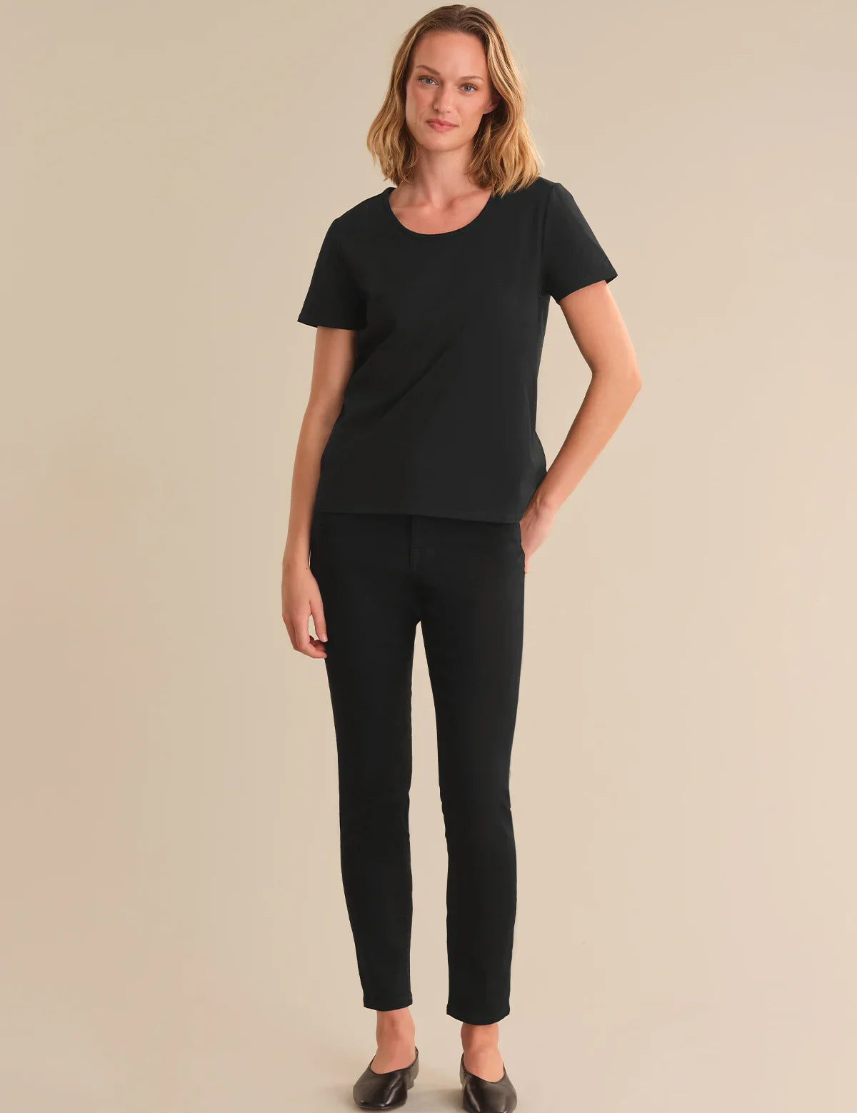 Woman wearing a black t-shirt and black pants on a beige background