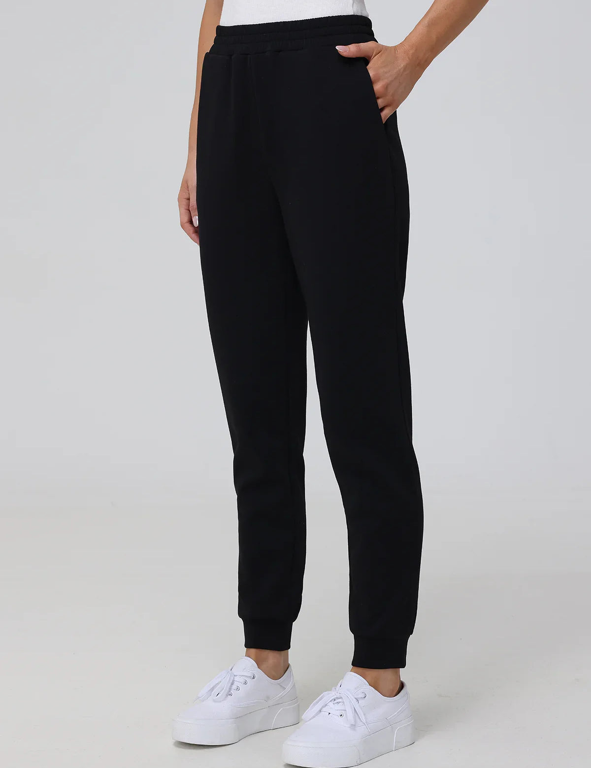 Person wearing black sweatpants and white sneakers on a plain background