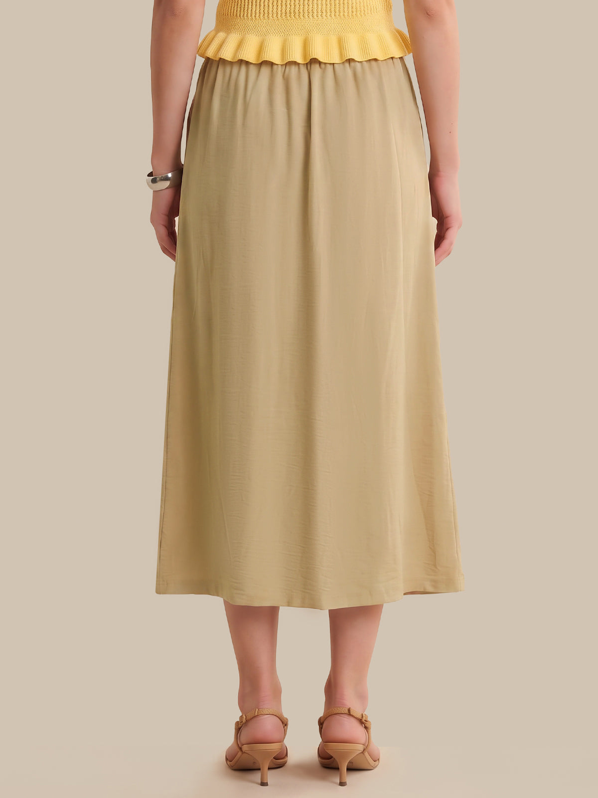 Person wearing a yellow top and beige skirt on a beige background