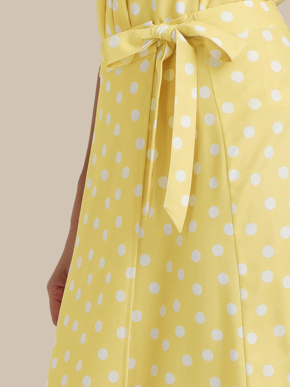 Yellow dress with white polka dots and a tie waist on a beige background