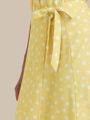 Yellow dress with white polka dots and a tie waist on a beige background
