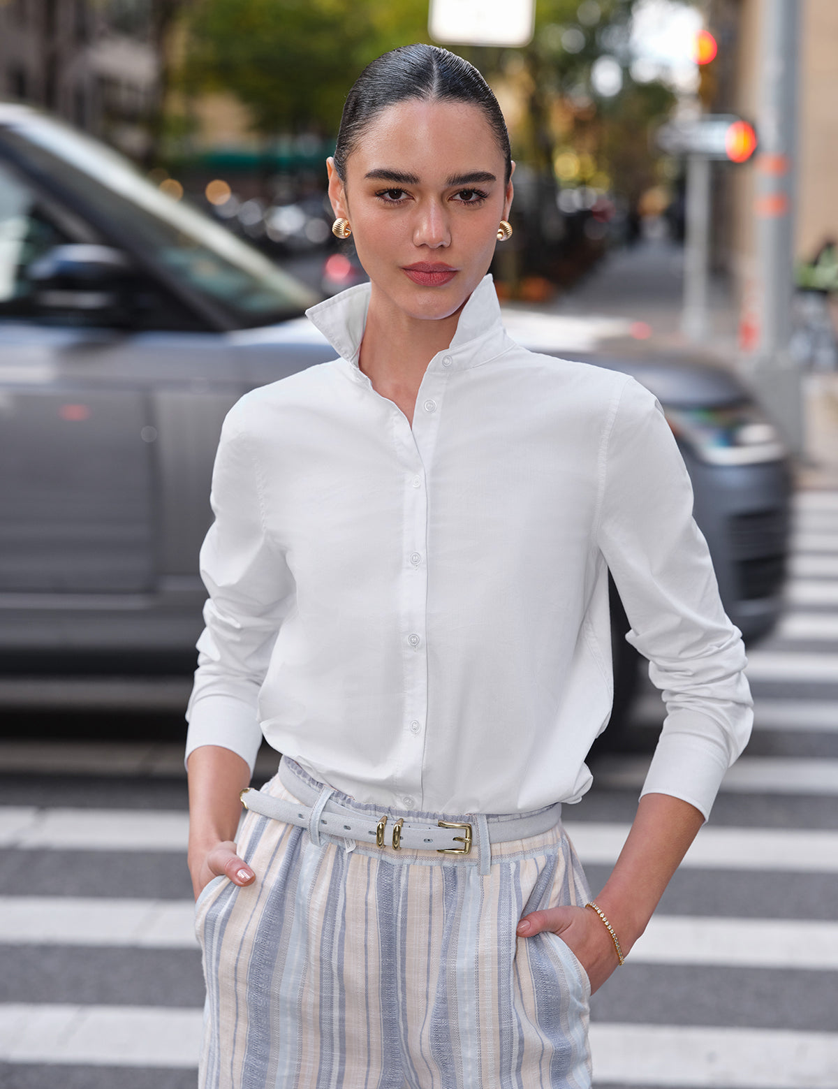 Woman in a white shirt and striped pants standing on a city street.