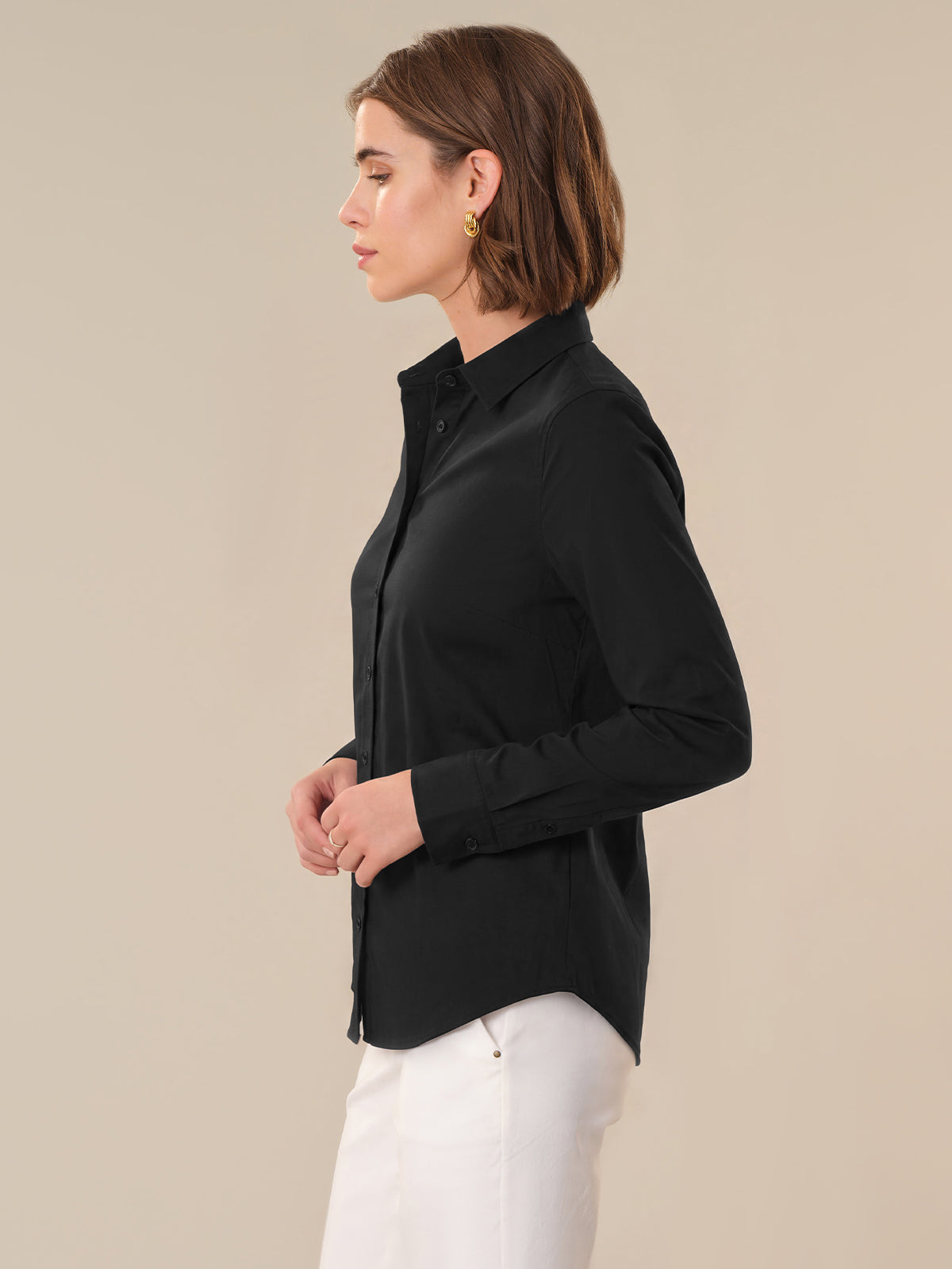 Woman wearing a black shirt and white pants against a beige background