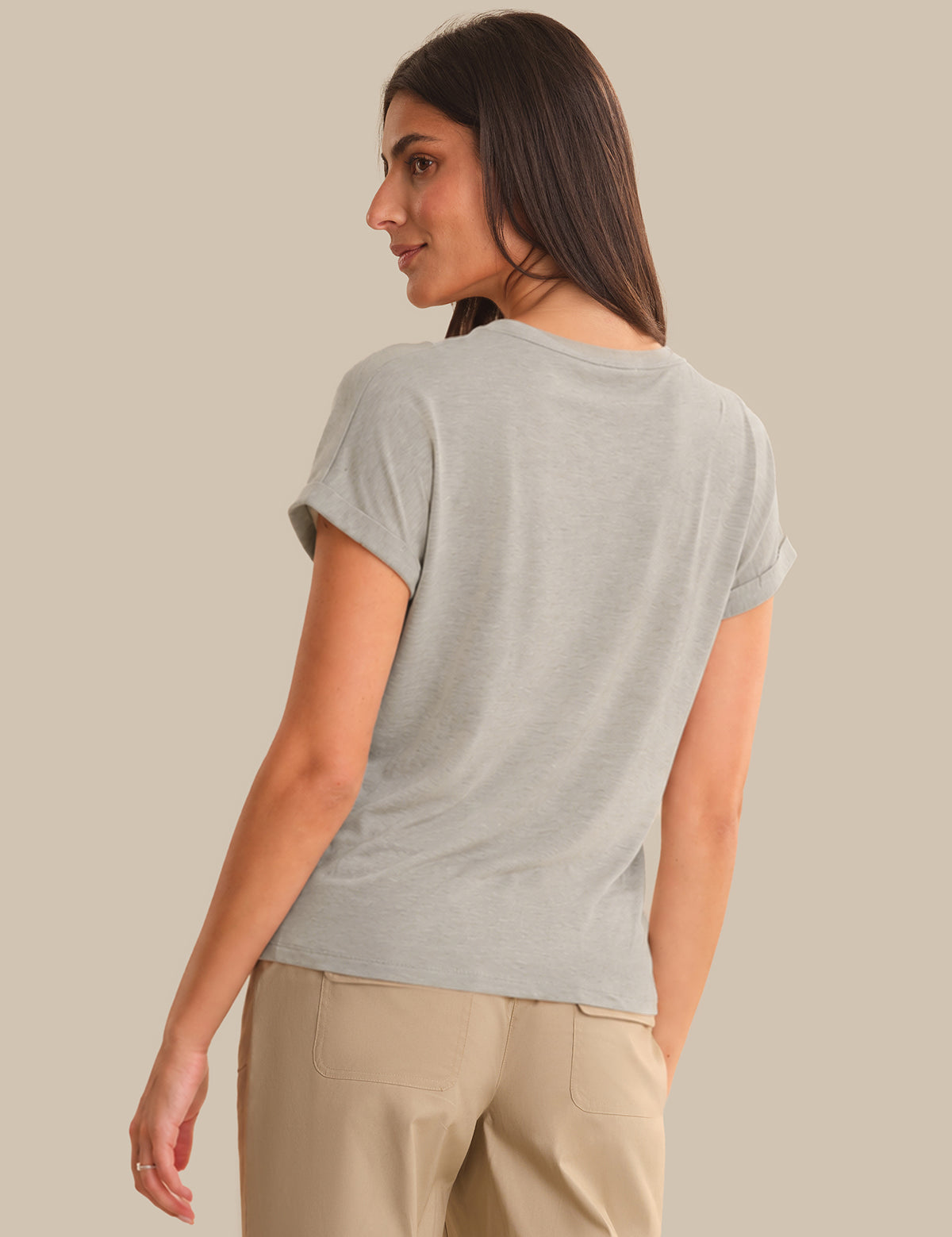 Woman wearing a light gray t-shirt and beige pants against a beige background
