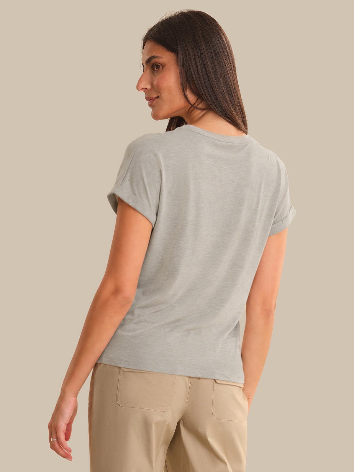 Woman wearing a light gray t-shirt and beige pants against a beige background
