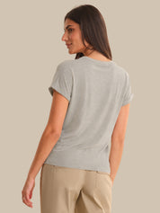 Woman wearing a light gray t-shirt and beige pants against a beige background
