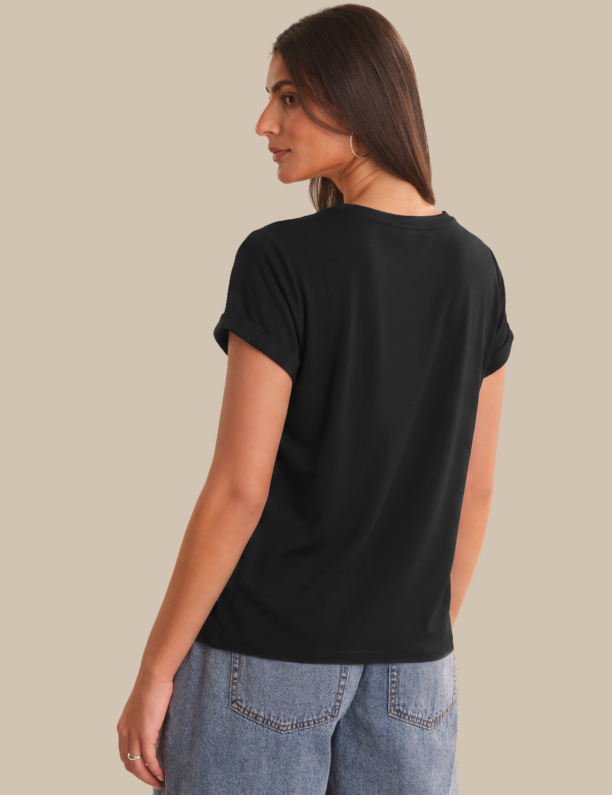 Woman wearing a black t-shirt and blue jeans on a beige background