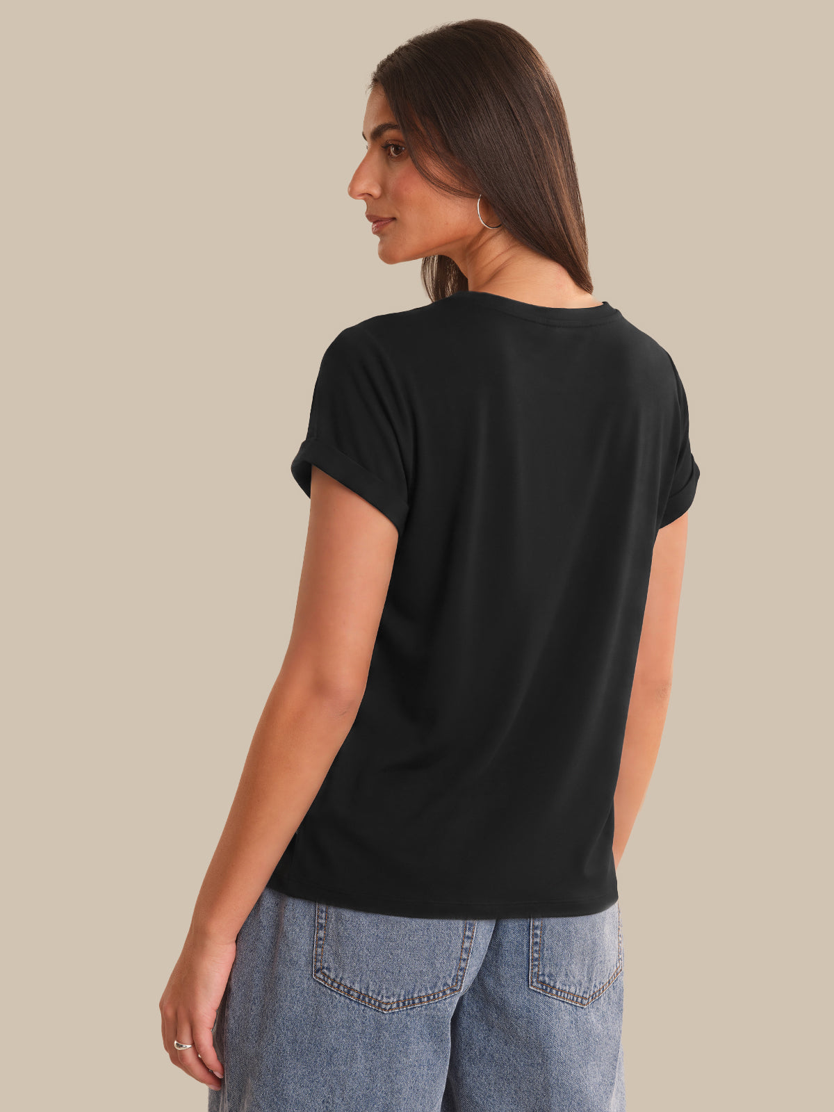 Woman wearing a black t-shirt and blue jeans on a beige background