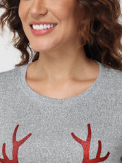Person wearing a gray sweater with red antler designs on a plain background