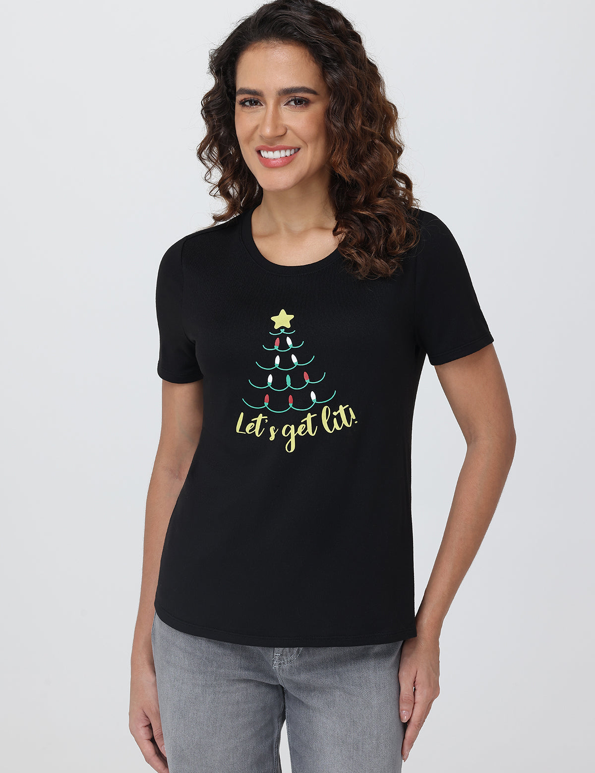 Woman wearing a black t-shirt with a Christmas tree design and text on a plain background