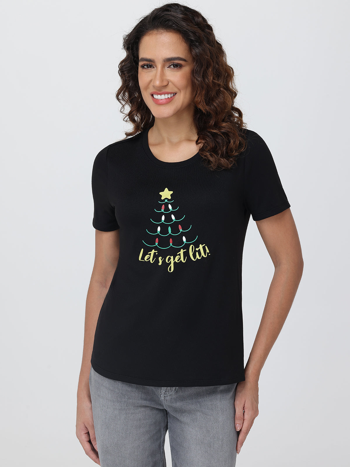 Woman wearing a black t-shirt with a Christmas tree design and text on a plain background