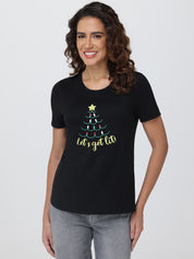 Woman wearing a black t-shirt with a Christmas tree design and text on a plain background