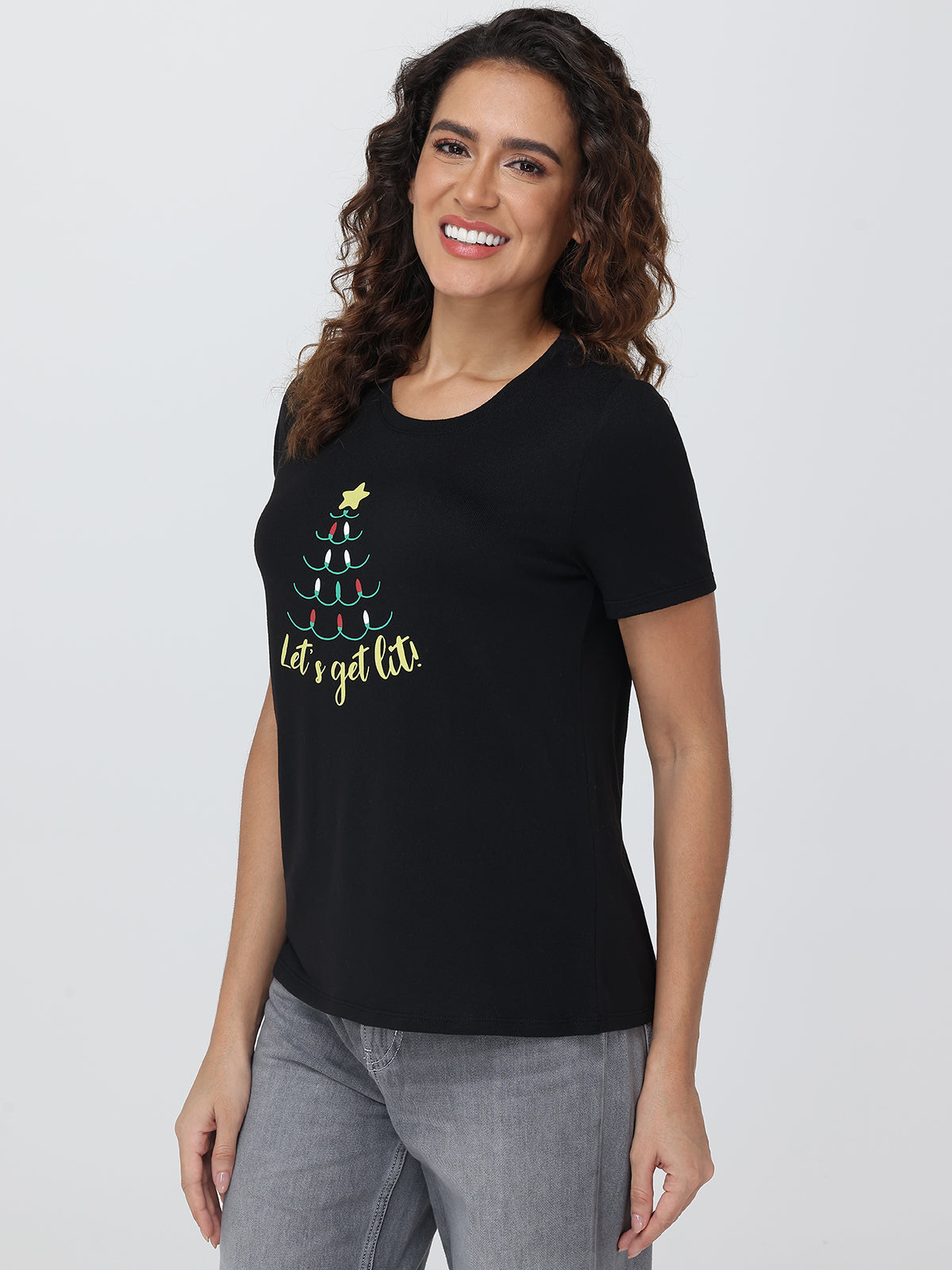 Woman wearing a black t-shirt with a Christmas tree design and text on a plain background