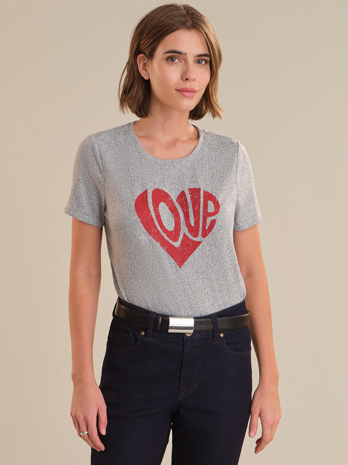Woman wearing a gray t-shirt with a red heart and 'LOVE' print on a beige background