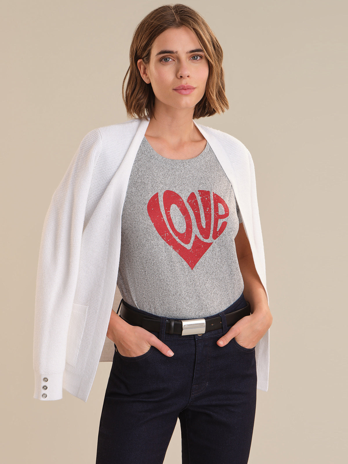 Woman wearing a gray t-shirt with a red heart and 'LOVE' text, paired with a white blazer and dark pants on a beige background.