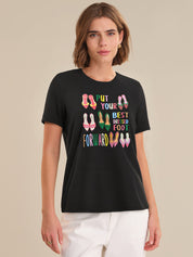 Woman wearing a black t-shirt with colorful text and shoe graphics on a beige background