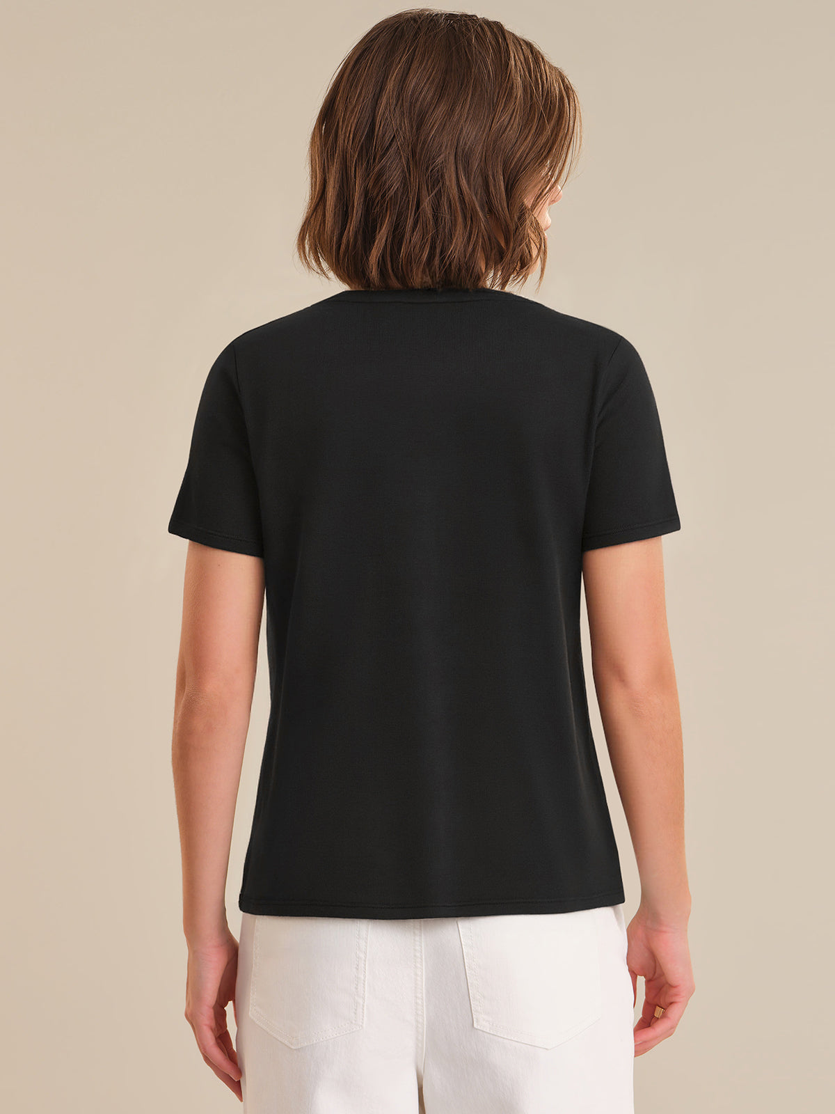 Person wearing a black t-shirt and white pants on a beige background